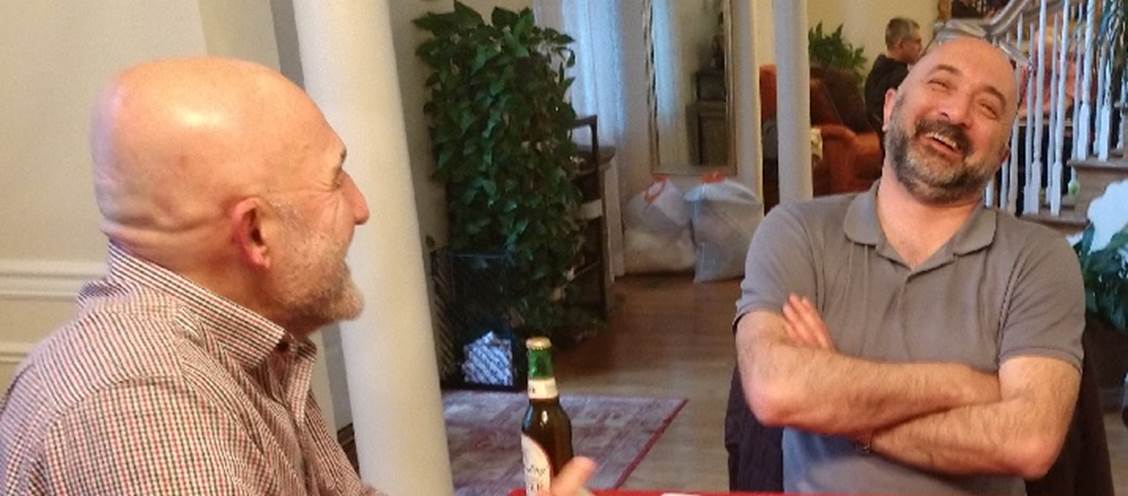 A couple of men sitting at a table with a bottle of beer

Description automatically generated with low confidence